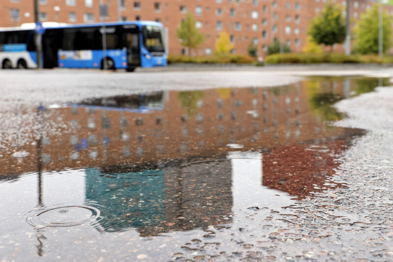 Kaupungin kadulla on vesilätäkkö. Taustalla ajaa bussi.