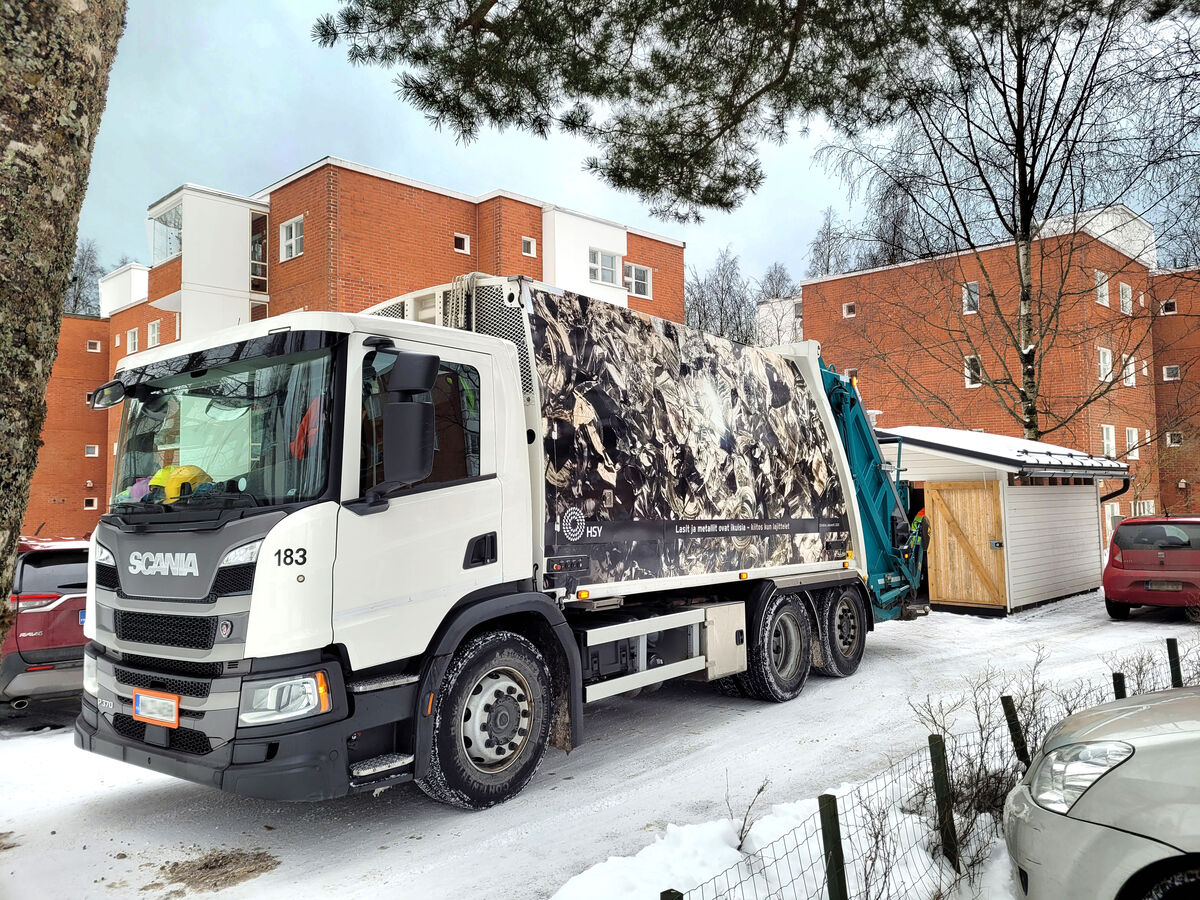 Jäteauto tyhjentää roskista taloyhtiön lumisella parkkipaikalla.